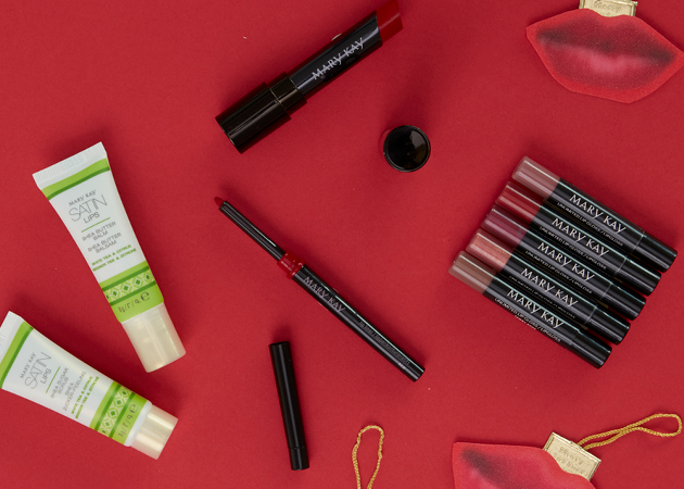 Produkte aus dem Mary Kay Geschenkset "Lovely Lips" zu Weihnachten liegen auf einem roten Untergrund