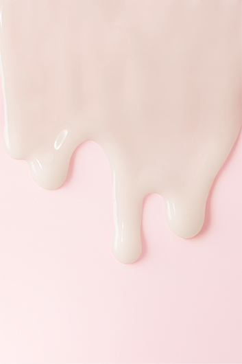 Auf einem rosafarbenen Hintergrund sieht man Tropfen einer Hautpflegecreme