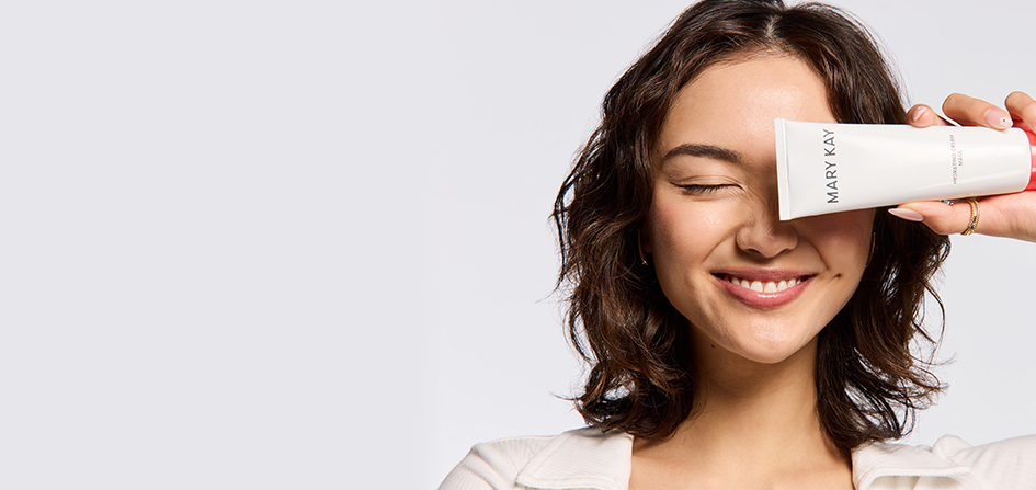 Eine Frau lächelt, hat ein Auge geschlossen und hält sich die neue Mary Kay Hydrating Cream Mask vor das andere Auge