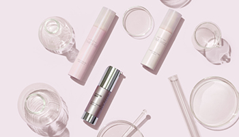 Drei Mary Kay Gesichtsseren und Reagenzgläser liegen schräg auf einer pinken Fläche