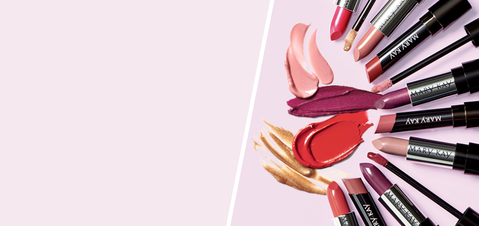 Verschiedene Mary Kay Hydrating Lipsticks, Semi Matte Lipsticks, Semi Shine Lipsticks und Ultimate Lipgloss liegen in einem Halbkreis auf einem rosa Untergrund – in der Mitte Smudges der Produkte.