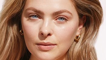 Eine Frau Anfang 20 mit strahlender, reiner Haut lächelt frontal in die Kamera