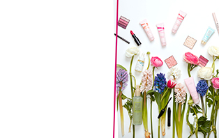 Mary Kay Geschenkideen zu Ostern 2022: über einer bunten Frühlingswiese mit blühenden Blumen schweben Mary Kay Produkte, die sich gut zum Verschenken eignen – Lippenstift, Rouge, Parfum, Handcreme, Lidschatten, Gesichtsöl, Highlighter, und vieles mehr