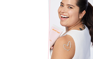  Eine Frau ist von hinten zu sehen. Sie lächelt über die Schulter, hält in einer Hand eine Tube der Mary Kay After Sun Body Lotion und auf ihrer Schulter ist mit weißer Lotion ein Herz gemalt.