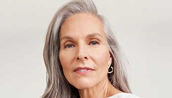 Eine Frau über 60 mit reifer, gepflegter Haut und einem Kurzhaarschnitt lächelt seitlich in die Kamera