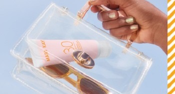 Bild eines Models, das eine durchsichtige Handtasche mit einer Tube der Mary Kay® Mineralische Sonnenpflege LSF 30 und einer Sonnenbrille vor blauem Hintergrund in der Hand hält 